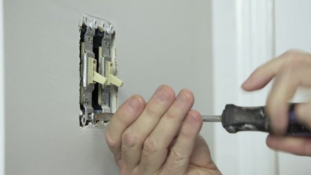 An electrician or homeowner handyman type removing an old toggle wall switch.