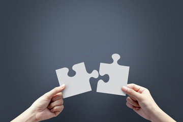 Close up of hands holding jigsaw on dark background.