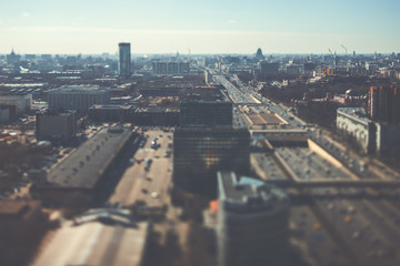 Fototapeta premium True tilt shift shooting of highway in metropolis from high above: multiple residential and office buildings, road intersection in focus with many cars on busy streets of the city, crosstown traffic