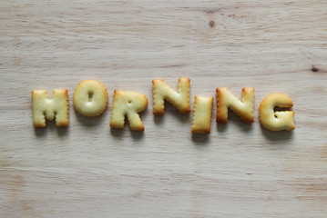 An inscription from the cookies on the wooden background. Text – morning.