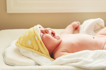 Obraz na płótnie Canvas Closeup portrait of crying screaming newborn baby child lying on changing table, covered wrapped in towel after taking bath, lifestyle real emotions concept