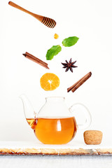 Flying ingredients of hot herbal tea with citrus, mint, cinnamon sticks, anise star and honey. White background.