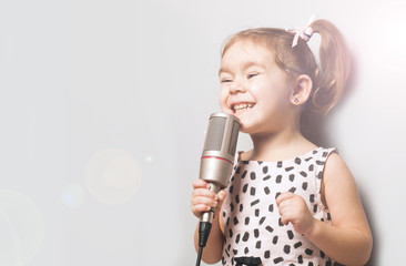 Happy Cute little girl singing a song on microphone. Grey background