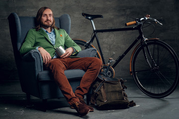 Fototapeta na wymiar A man dressed in a green jacket sits on a chair with single speed bicycle on background.