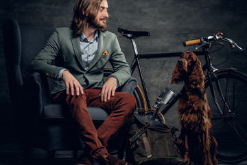 Stylish male with long hair posing with Ireland setter and single speed bicycle.