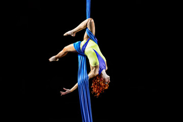 Beautiful young, athletic sexy woman professional aerial circus artist with redhead in yellow costume make coup in the air, light in the darkness. Dancing in the air with balance. © Alexander