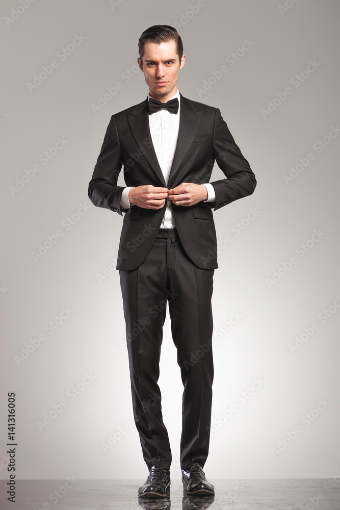 Wall mural sexy young man in tuxedo and bowtie buttoning his suit