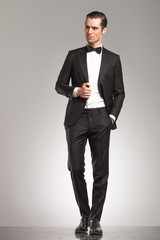 man in tuxedo  looks away while holding his colllar