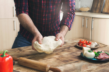 Man preparing pizza in home kitchen on wooden table