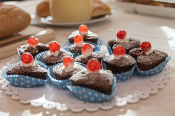 Close up of chocolate muffins with red cherry. Bread in the background. Breakfast time