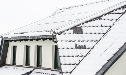 schneebedecktes Dach mit Gaube und vier Fenstern belegt mit Photovoltaikanlage im Winter 