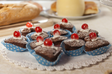 Close up of chocolate muffins with red cherry. Bread in the background. Breakfast time