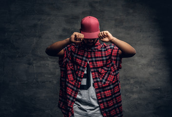 Black bearded male dressed in a red fleece shirt and a cap. - obrazy, fototapety, plakaty