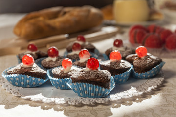 Close up of chocolate muffins with red cherry. Bread in the background. Breakfast time in a italian bed and breakfast