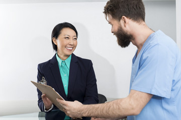 Receptionist And Doctor Discussing Over Clipboard