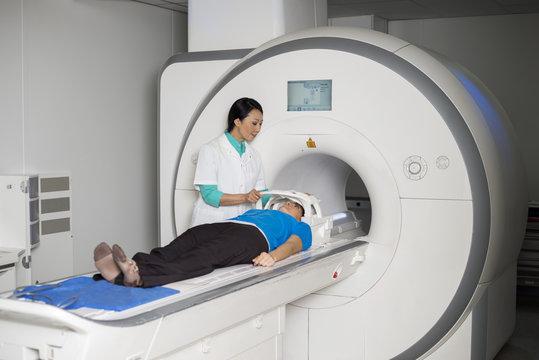 Doctor Fixing Mask To Patient Lying On CT Scan Machine