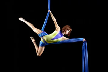 Beautiful young, athletic sexy woman professional aerial circus artist with redhead in yellow costume posing diagonal in the air, light in the darkness. Dancing in the air with balance. © Alexander