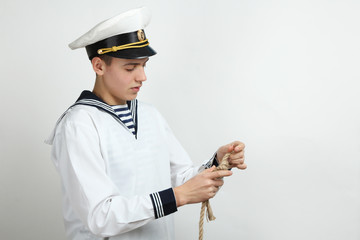 A young sailor ties up the sea knot on a neutral background.