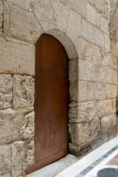 Angled view of  a wooden aged vaulted ornate door and stone wall, Medieval Cairo, Egypt