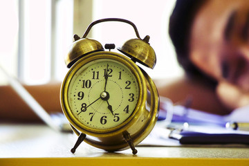 Alarm clock is on the table with working hard man blurry background