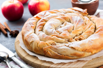 Round burek pie with an apple on a dark background. Traditional Serbian cuisine. Selective focus....