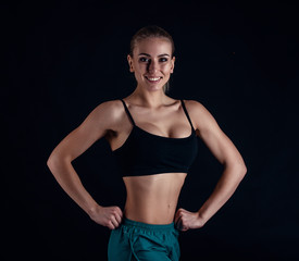 Obraz premium Sporty young girl in sportswear showing muscles on black background. Tanned young athletic woman. A great sport female body.