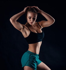 Fototapeta na wymiar Sporty young girl in sportswear showing muscles on black background. Tanned young athletic woman. A great sport female body.