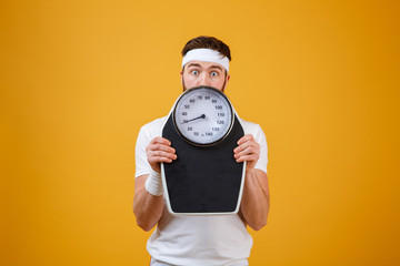 Portrait of a young fitness man hiding behind weight scales