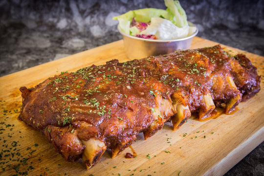 Grilled rib pork with barbecue sauce and vegetable on wooden cutting board.