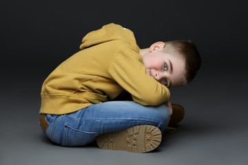 Handsome little boy in jeans sitting on floor