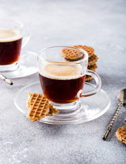 Glass cups of coffee with mini stroopwafel, syrupwaffles cookies on light gray background with copy space.