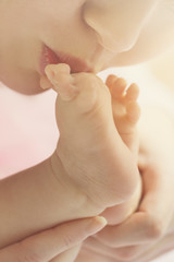 Naklejka premium Mother kisses baby feet, closeup. Daylight. Selective focus.