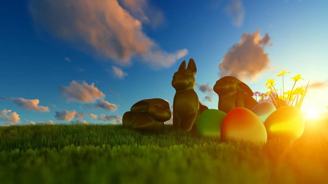 Easter Eggs and Chocolate Bunnies on green meadow against beautiful sunrise