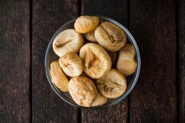 Dried figs in glass bowl on wooden background.