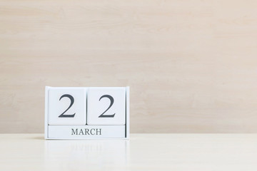 Closeup surface white wooden calendar with black 22 march word on blurred brown wood desk and wood wall textured background with copy space , selective focus at the calendar