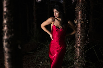 Beautiful young woman in the gardens wearing a long silk red dress.