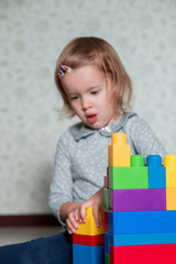 Child girl having fun and build of bright plastic construction blocks. Toddler playing on the floor. Developing toys. Early learning.