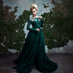 Fototapeta premium Portrait of young attractive blonde woman in a beautiful green dress. Textured background, interior. Luxury hairstyle