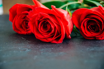 Three red roses over black stone background. Copy space. Close up.