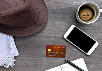 Mobile smart phone, credit card, notebook, hat mad of fabric and a cup of coffee on wood texture background.