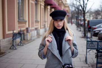 Young, hip and attractive blonde walking around the city, girl in a stylish hat and a gray coat