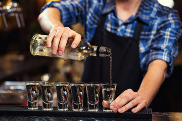 Barman at work,Barman pouring hard spirit into glasses in detail,Bartender is pouring tequila into glass,preparing cocktails,concept about service and beverages
