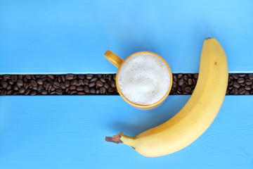 reinforcement appetizing coffee breaks morning/ flat layout with a yellow mug of frothy cappuccino on a blue table with fried beans and banana 
