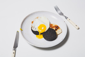 Fried egg with black pudding and cutlery on white background