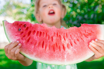 Big slice watermelon in unrecognizable little girls hands in summer time in park, outdoor. Close up.