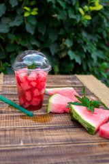 Watermelon cocktail with slice on wooden background, outdoors.