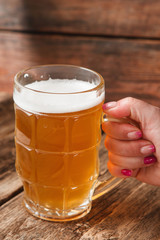 Unrecognizable person holding mug with light beer in bar on wooden rustic table background. Close up view.