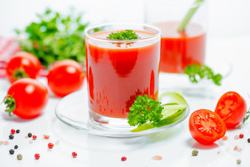red tomato juice in transparent glasses with parsley, cutted tomato fruit, cucumber and dry pepper,...