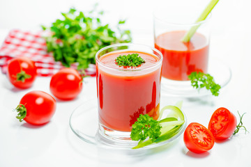 tomato juice in transparent glasses with parsley, cutted tomato fruit, cucumber and red napkin, close up