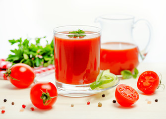 tomato juice in glass, jug with greenery, basil, cutted tomato fruit and dry pepper on light table, concept vegetarian food, close up